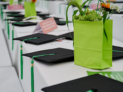 On a table covered with a white tablecloth are graduation hats and bouquets of flowers in green paper bags.